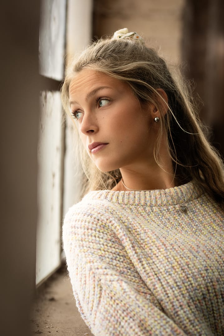 Frau in hellem Pullover sitzt am Fenster und blickt nach rechts ins Licht